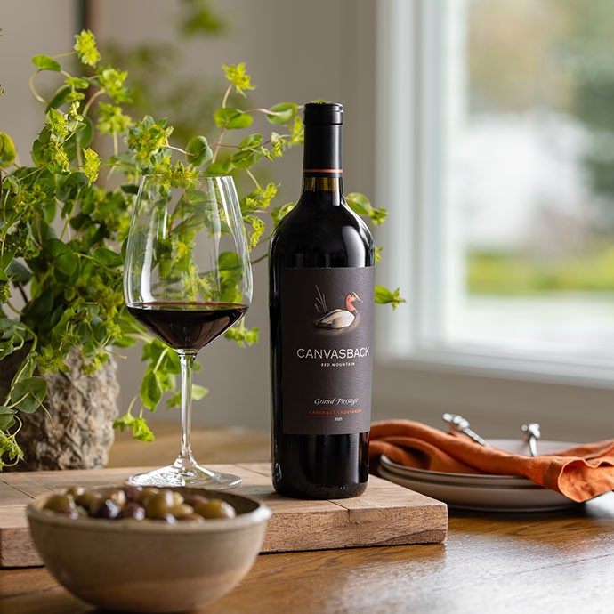 A bottle of Canvasback Grand Passage wine on the counter next to a bowl of olives